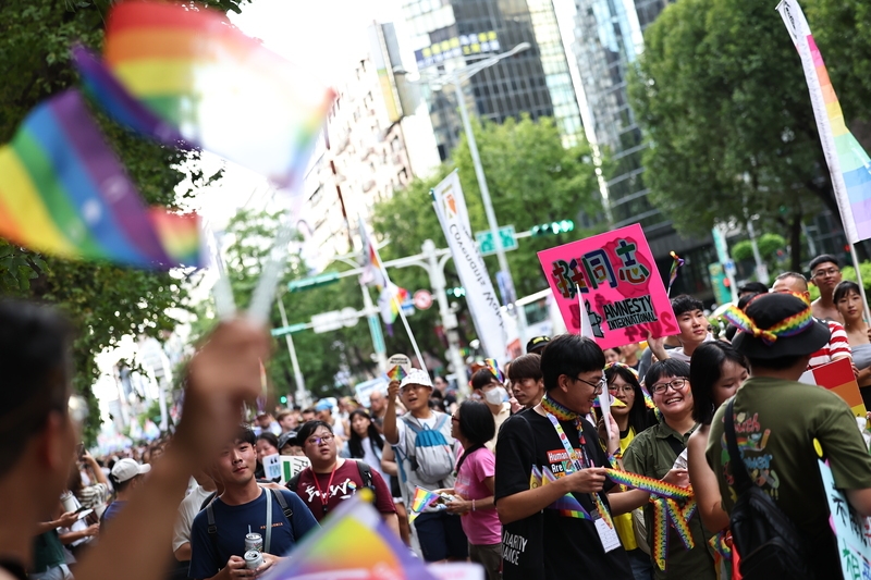 2024第22屆台灣同志遊行26日下午在台北街頭熱鬧展開，邀請海內外彩虹公民一起「邁向共融，交織共生」，有民眾揮舞彩虹旗、拿著「挺同志」標語開心參與。（中央社提供）